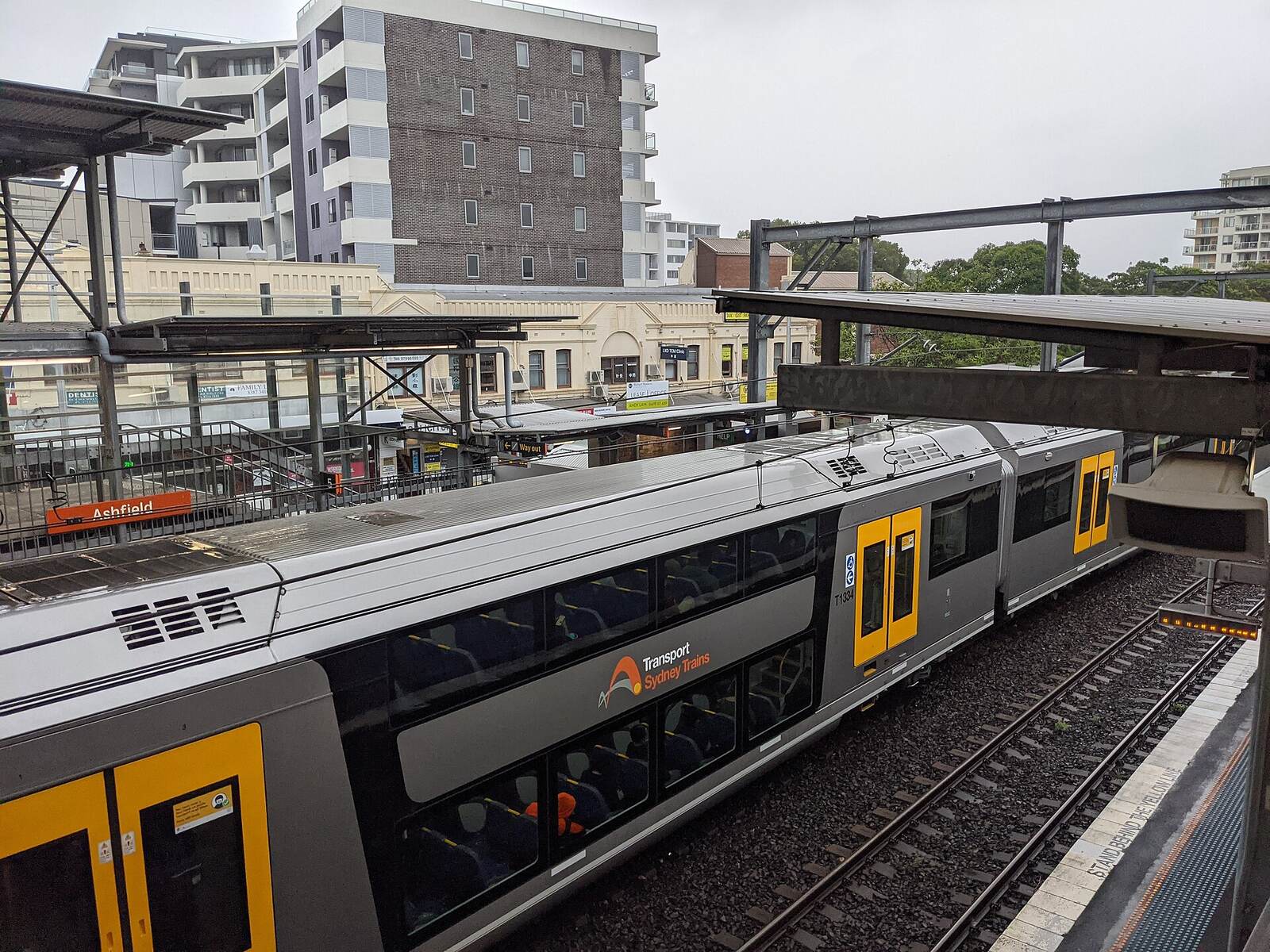 Sydney Trains double-decker at Ashfield station seen from above, with apartment buildings behind