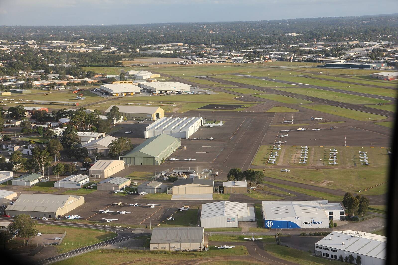 Aerial view of Bankstown Airport hangars, parked light aircraft and runways stretching into the suburbs