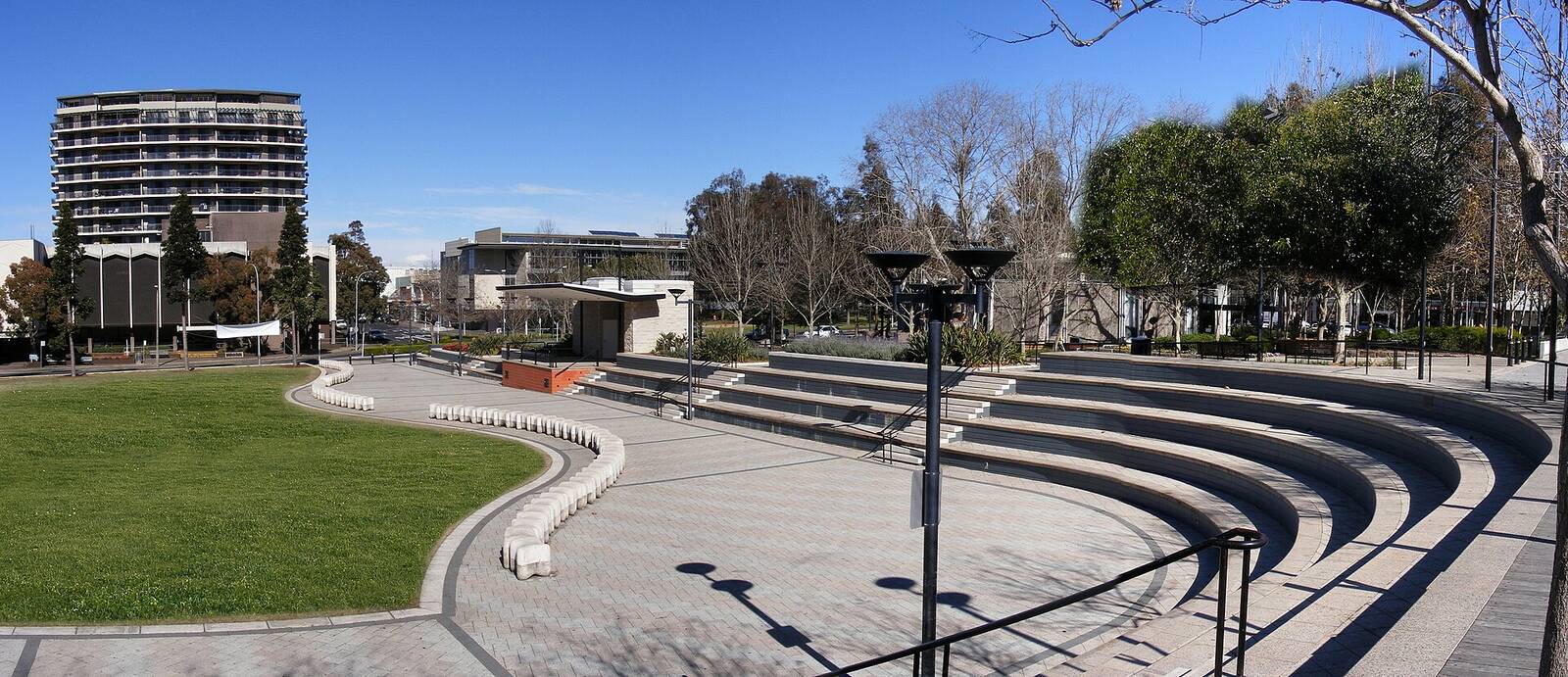 Curved concrete seating steps and lawn in Paul Keating Park, Bankstown, with apartments behind