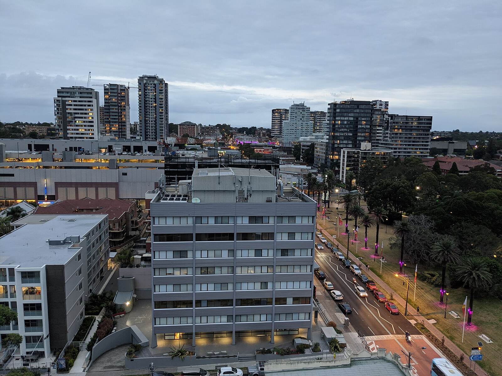 Burwood apartment towers and a tree-lined road with lights coming on at dusk