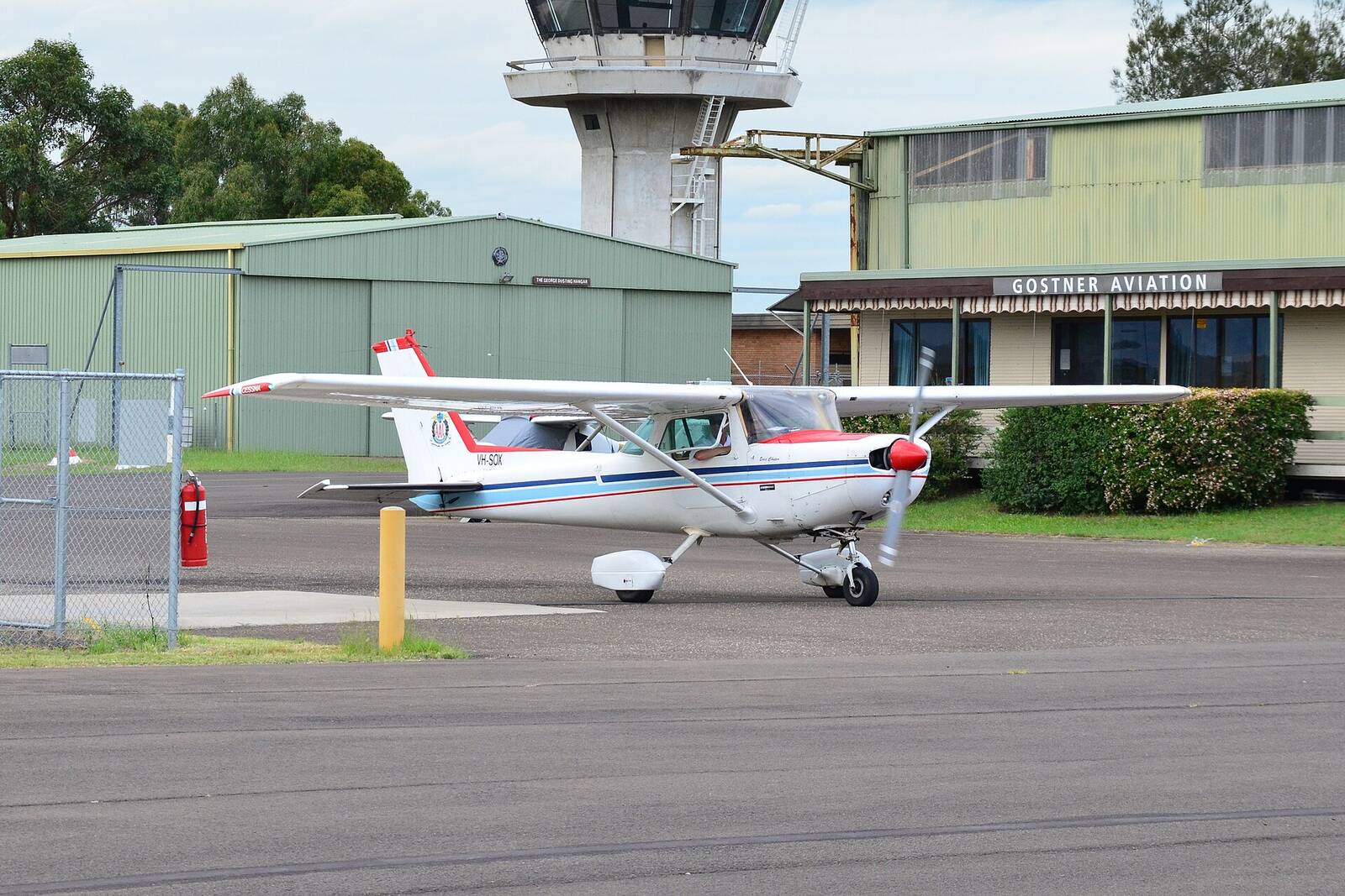 Small Cessna training plane parked outside a hangar at Camden Airport, with the control tower behind