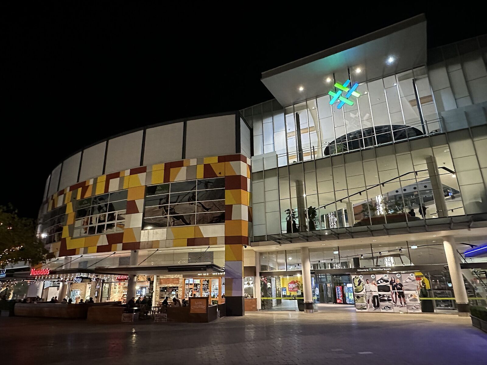 Macarthur Square shopping centre entrance lit up in the evening, with restaurants at street level