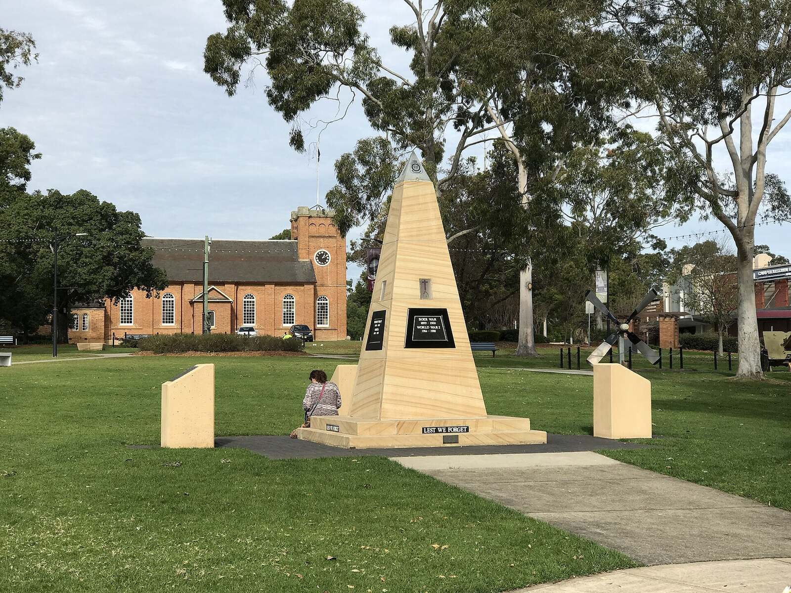 Sandstone war memorial in Mawson Park, Campbelltown, with St Peter's Church and gum trees behind