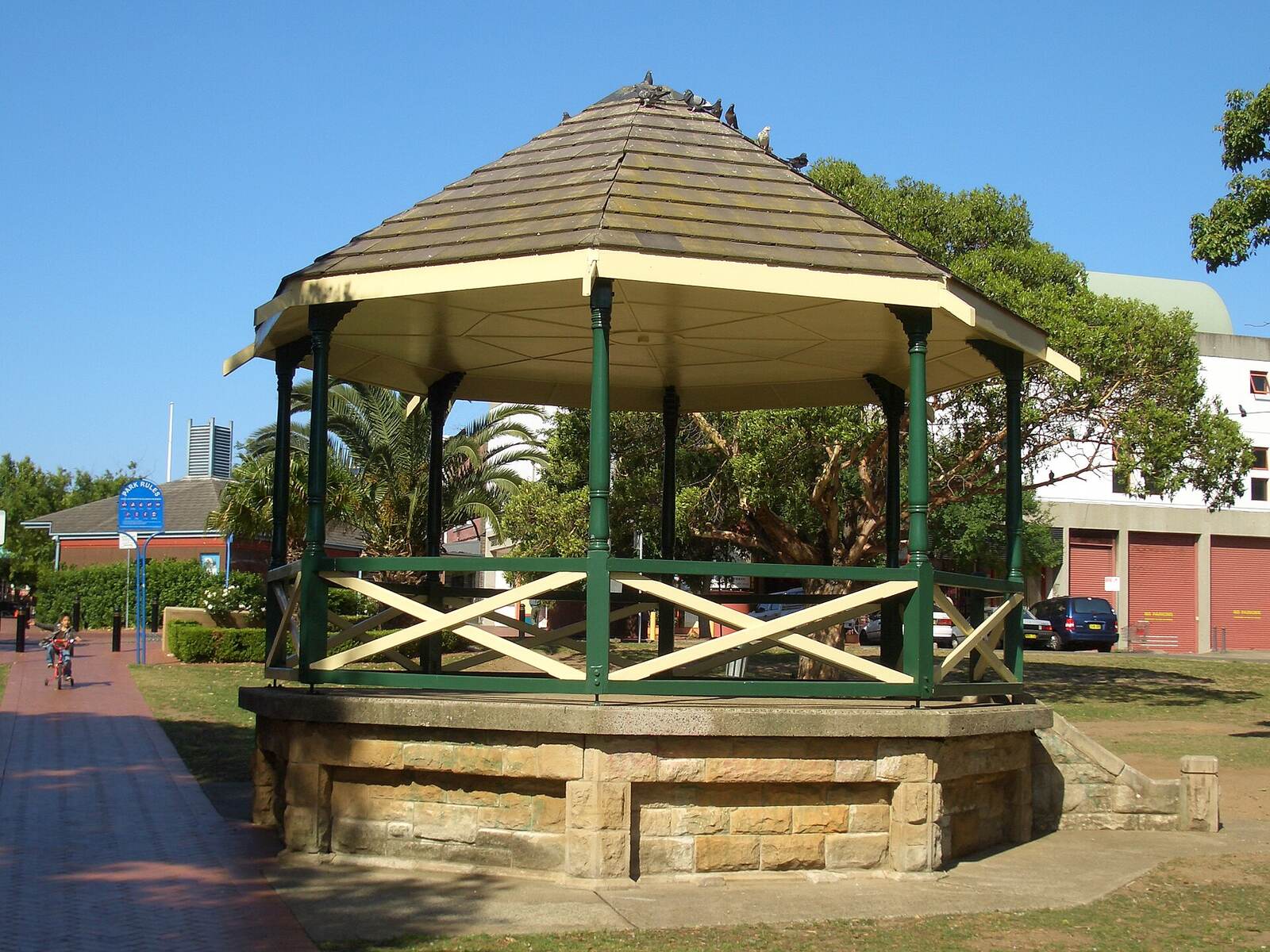 Green and cream rotunda on a sandstone base in a Campsie park, with trees behind