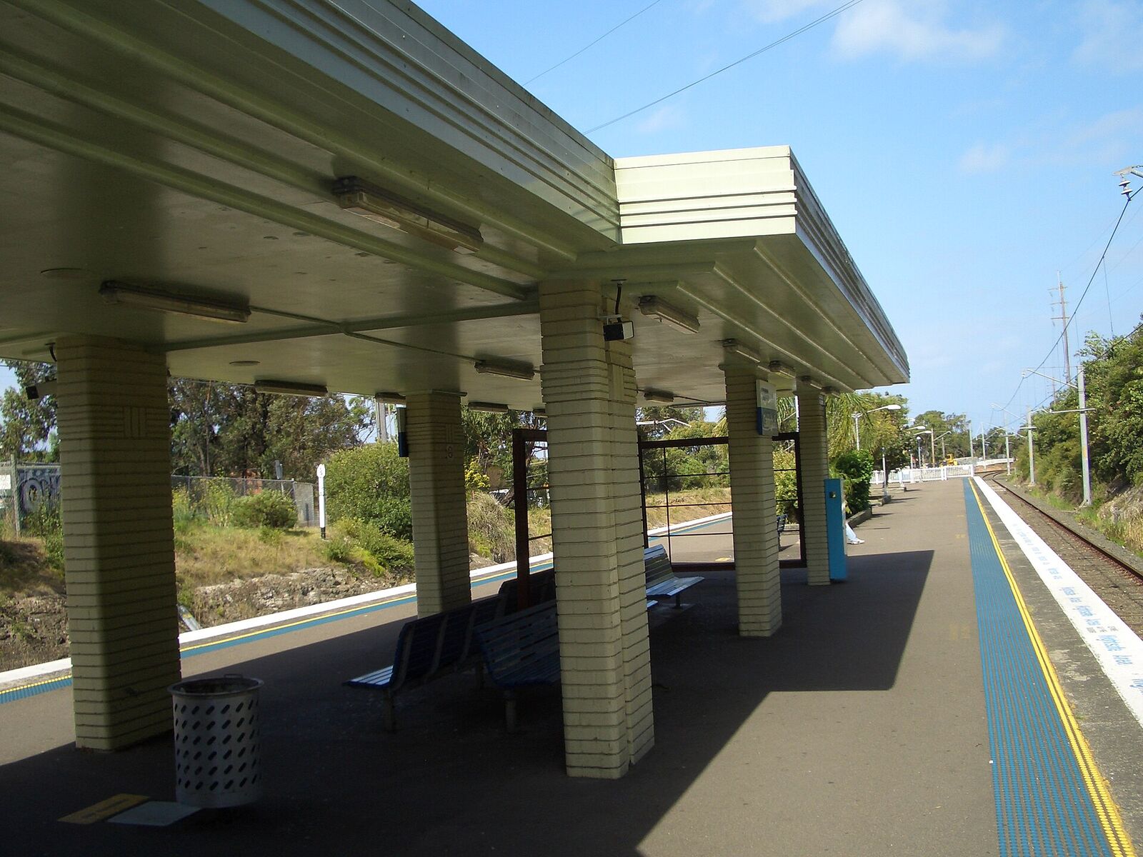 Covered island platform at Caringbah railway station with cream brick columns and blue benches