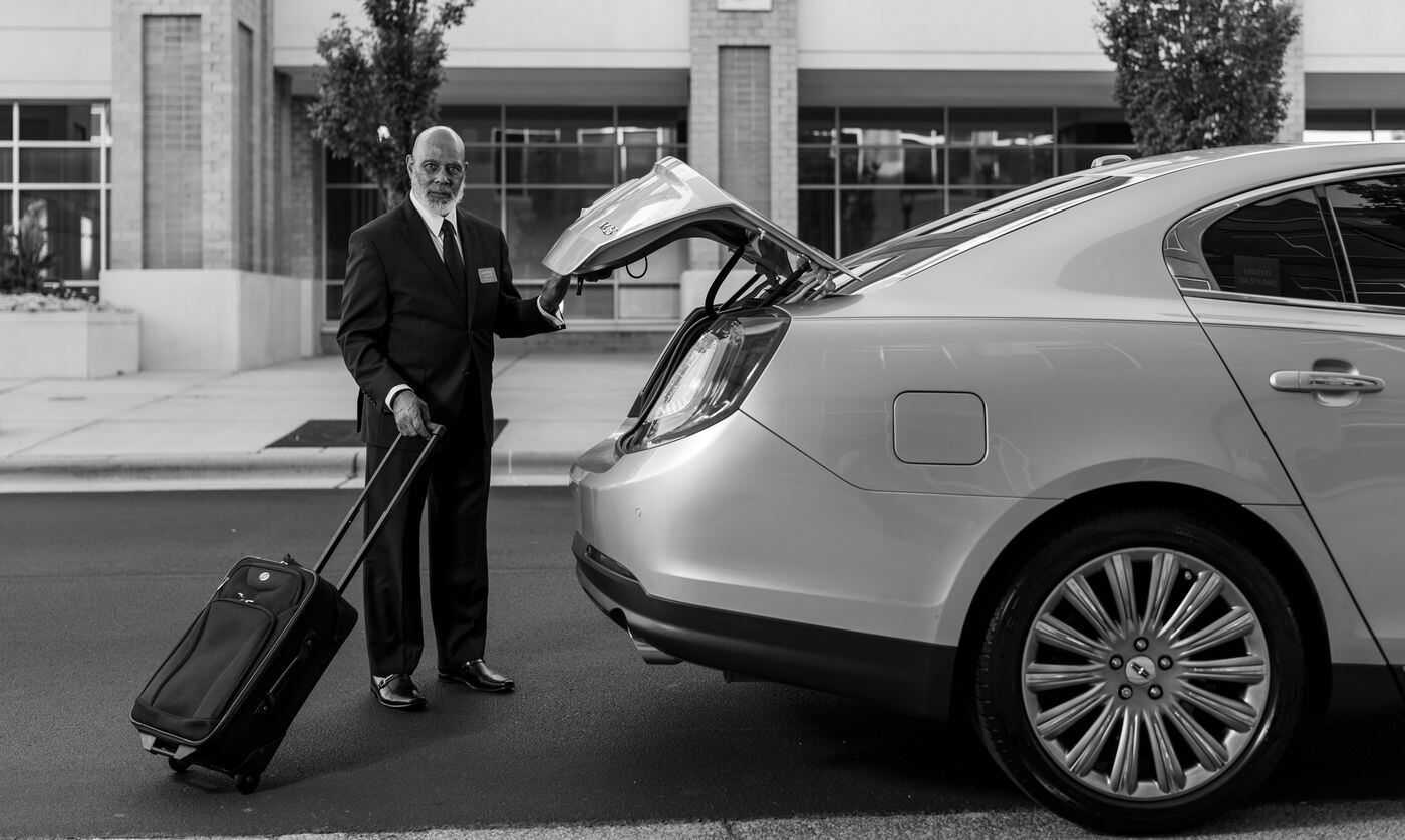Chauffeur in a suit loading a suitcase into the boot of a silver sedan