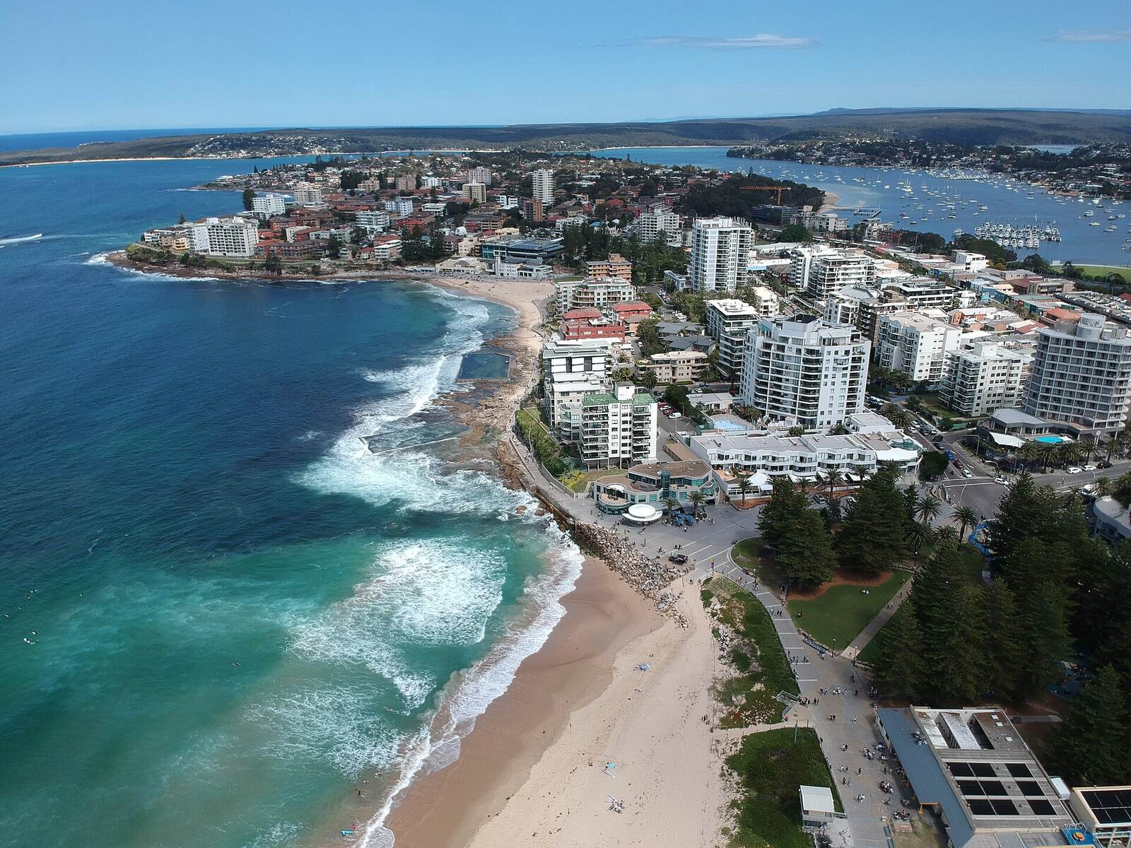 Aerial view of Cronulla Beach, the ocean pools and apartment towers on the point, with Gunnamatta Bay and Port Hacking behind