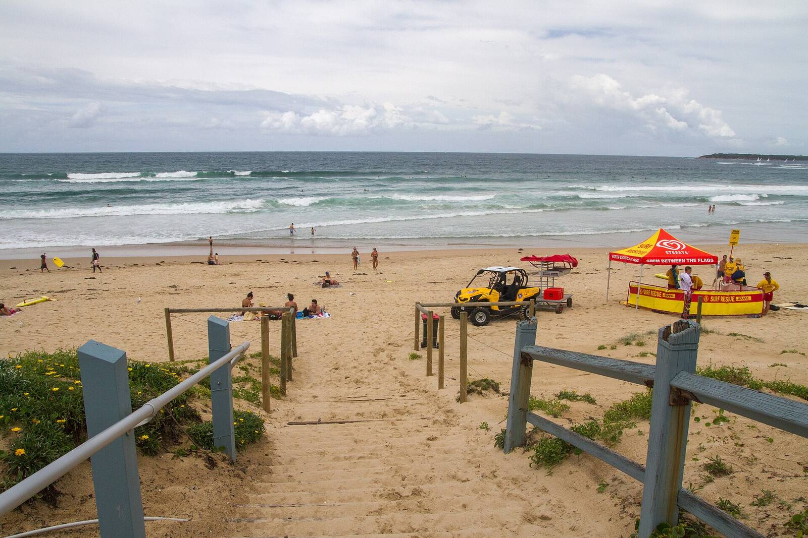Sandy beach access track onto North Cronulla Beach, with a lifesaving tent and buggy near the flags