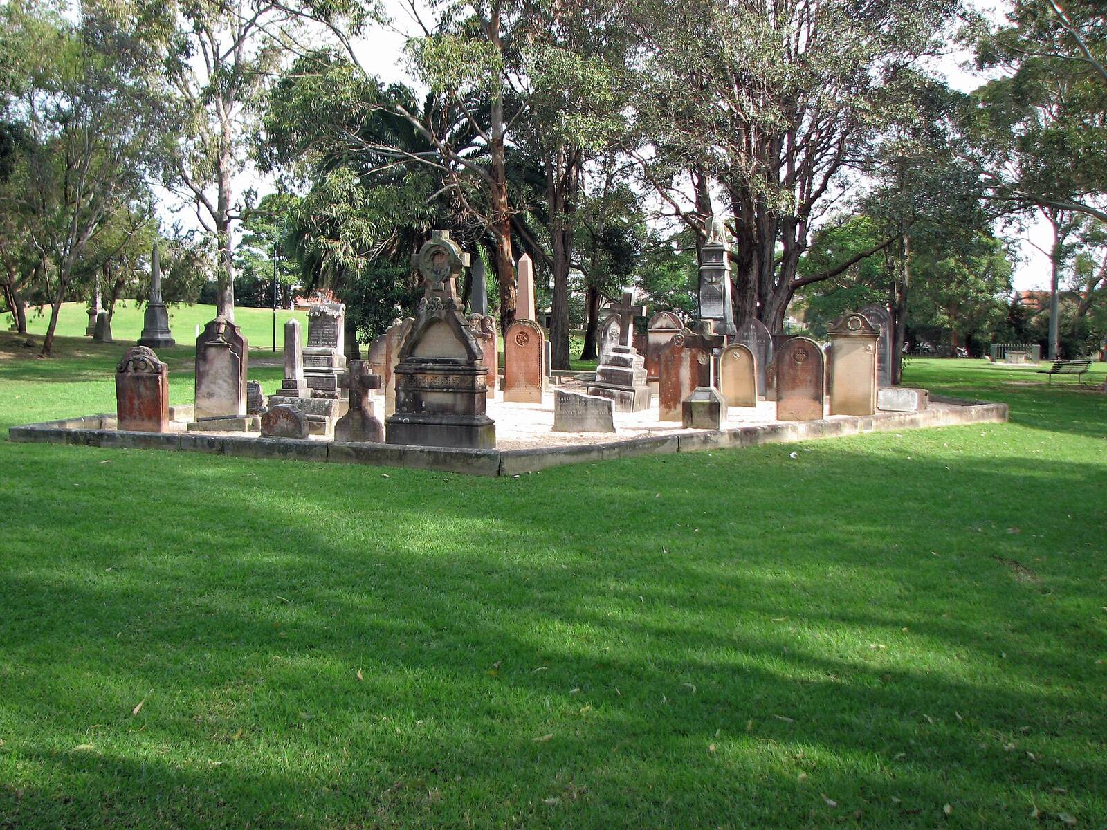 Old sandstone headstones grouped on the lawn under tall trees in St Thomas Rest Park, Crows Nest