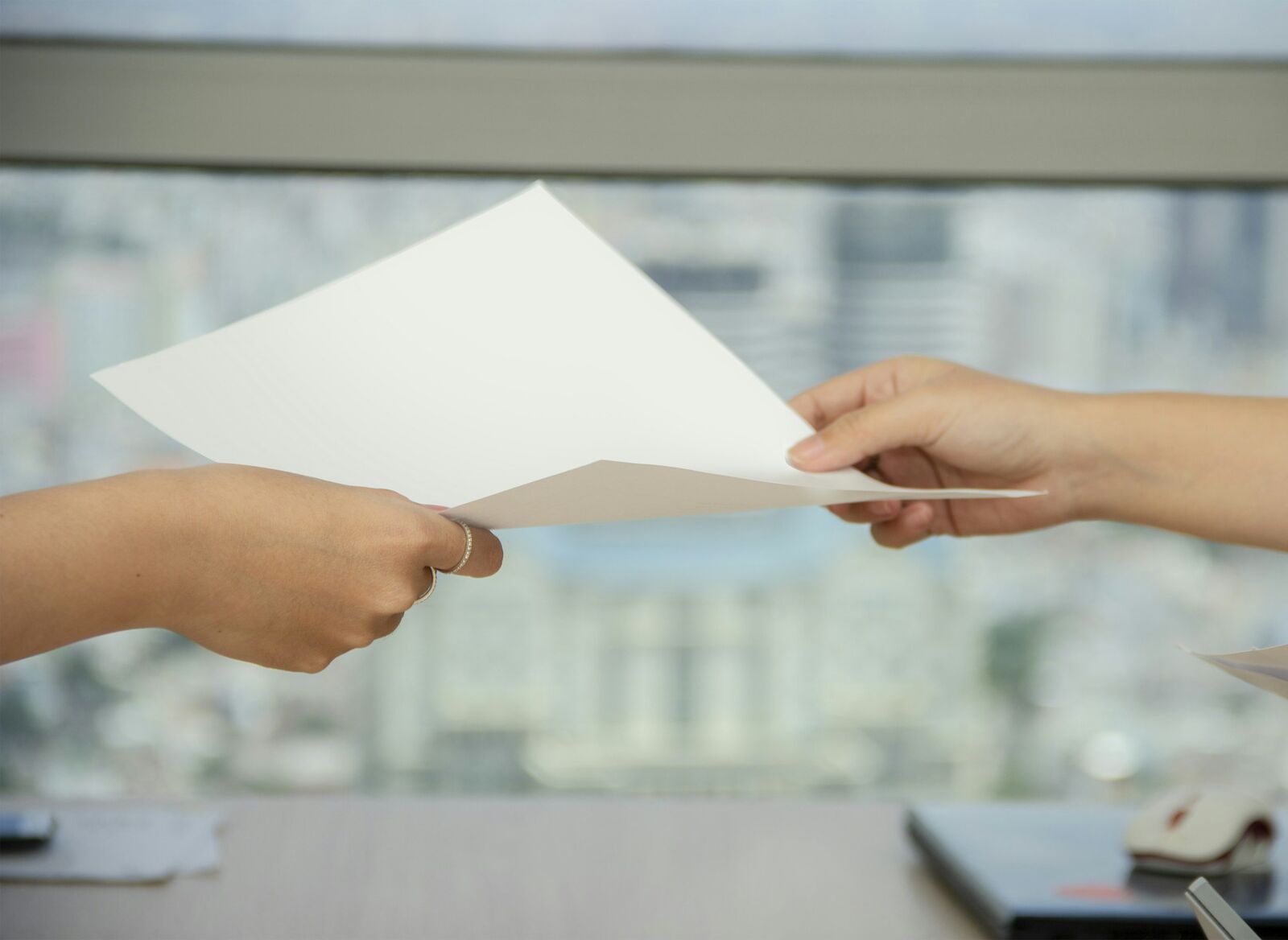 One person handing a sheet of paper to another across an office desk