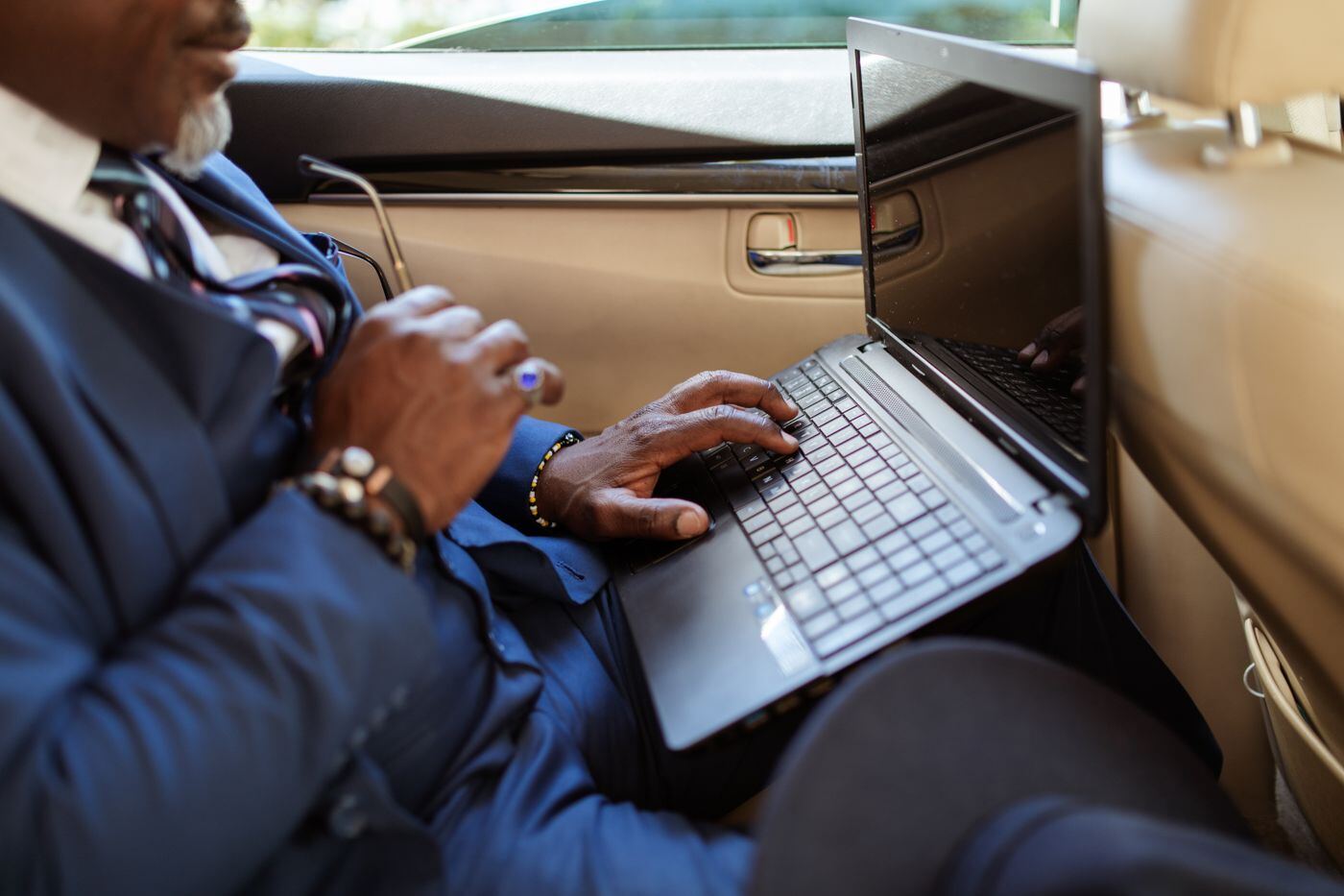 Executive in a suit typing on a laptop in the back seat of a car