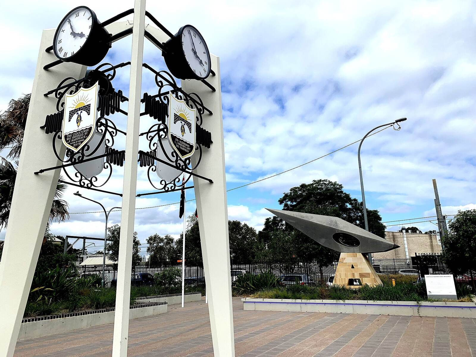 Twin clock faces and coats of arms on the white clock tower in Crescent Park, with the International Monument behind