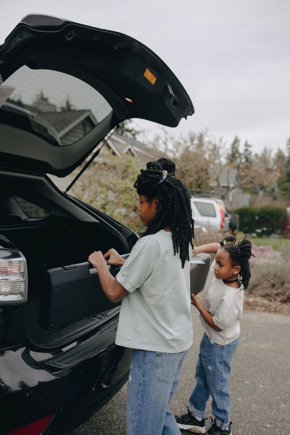 Two young girls lifting a bag into the open boot of a car