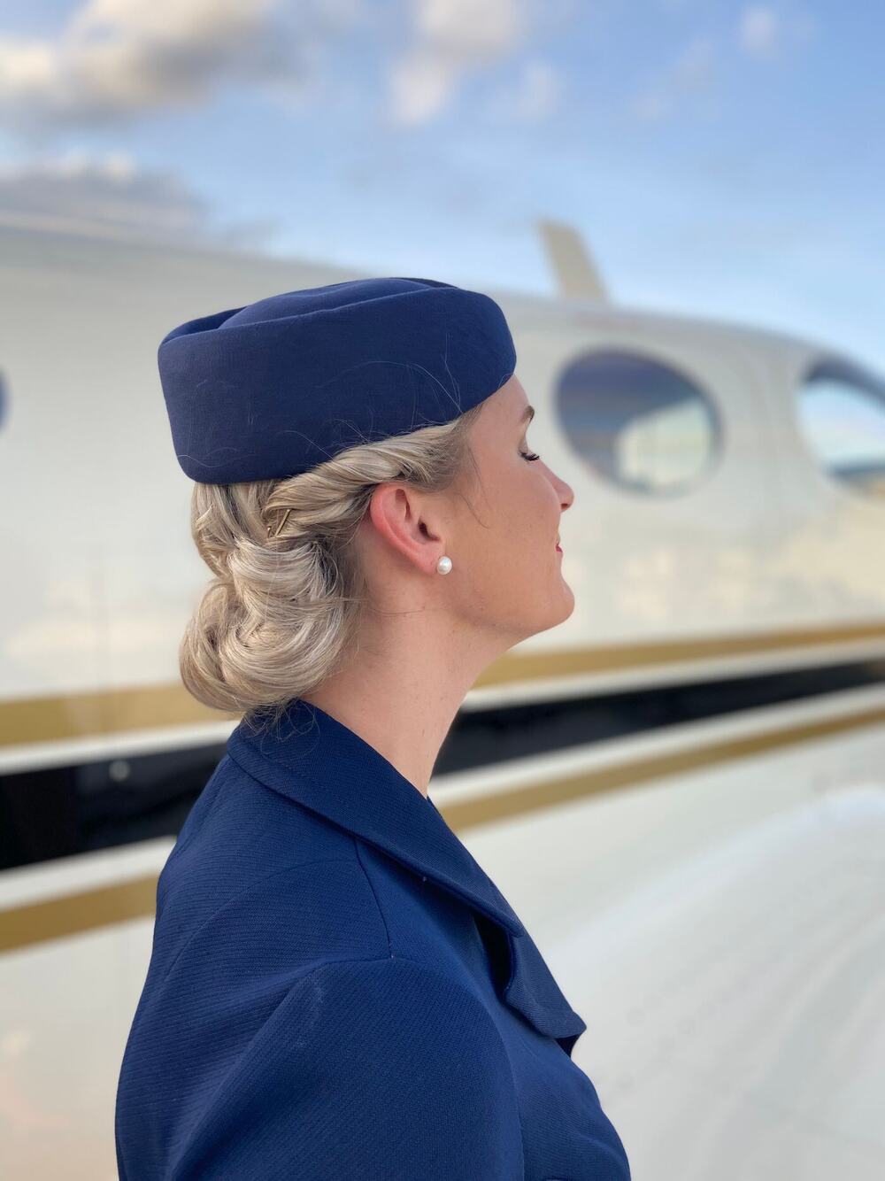 Flight attendant in a navy uniform and hat standing beside an aircraft