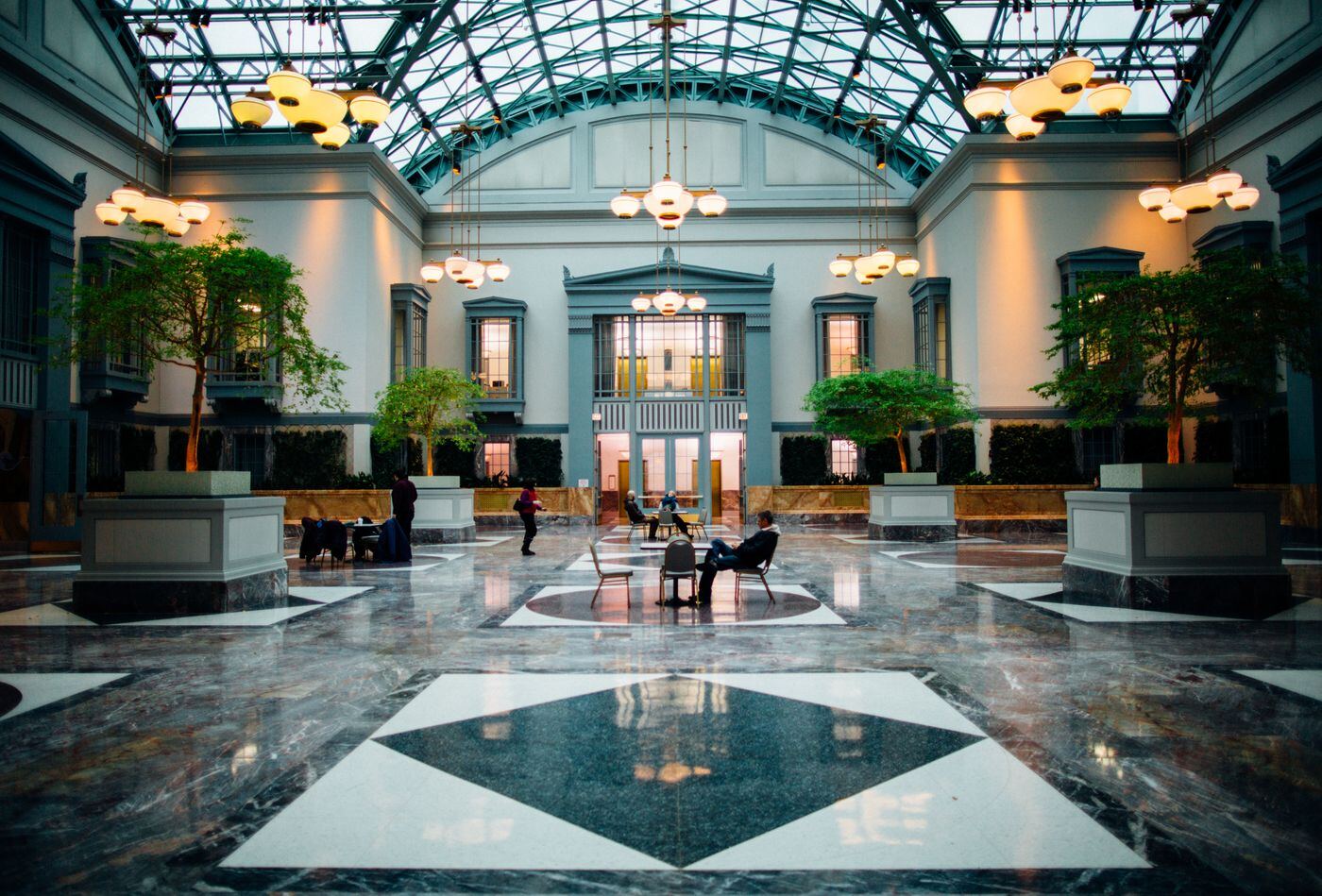 Glass-roofed hotel atrium with marble floors, potted trees and warm lighting