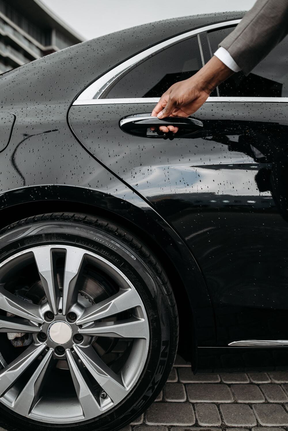 Suited arm reaching for the rear door handle of a polished black car