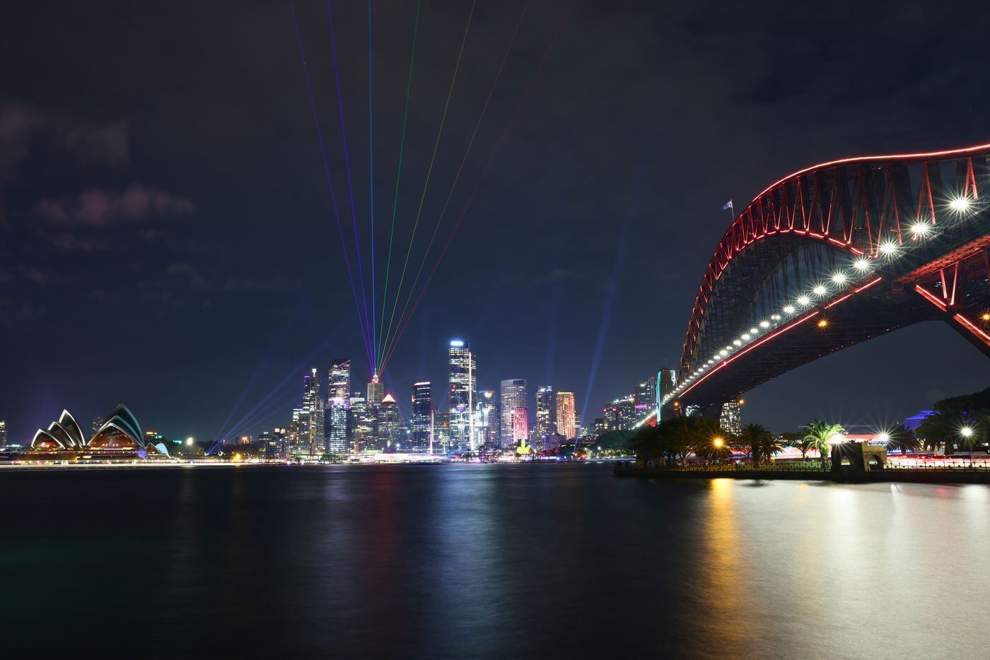 Sydney Harbour Bridge and city skyline lit up at night with light beams over the harbour