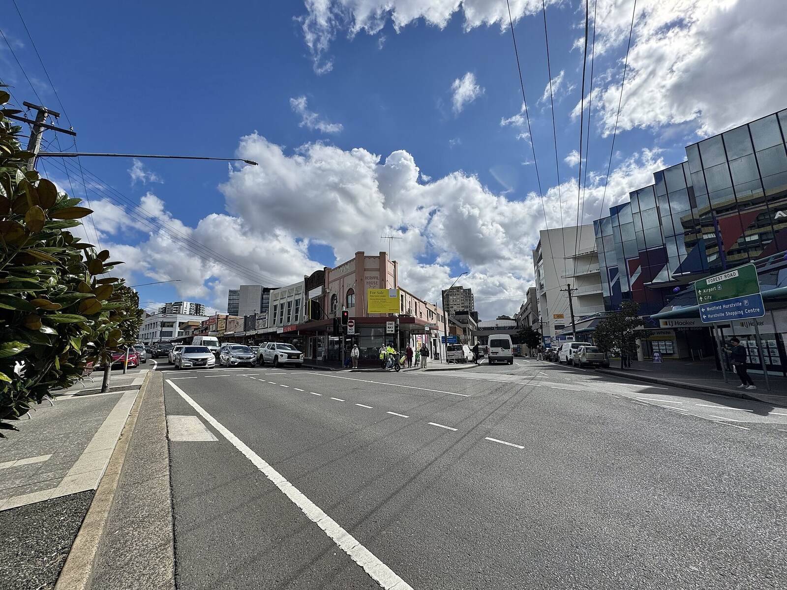 Forest Road in Hurstville at the Park Road intersection, lined with shops and office buildings under a cloudy blue sky