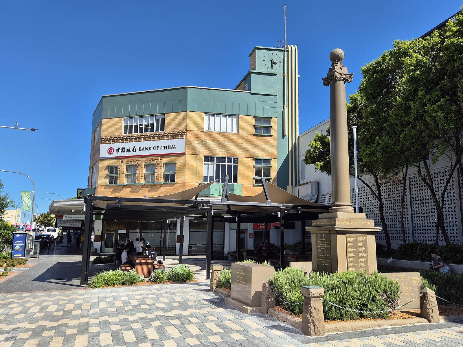 War memorial column in Hurstville Memorial Square, with shade sails and a clock tower building behind