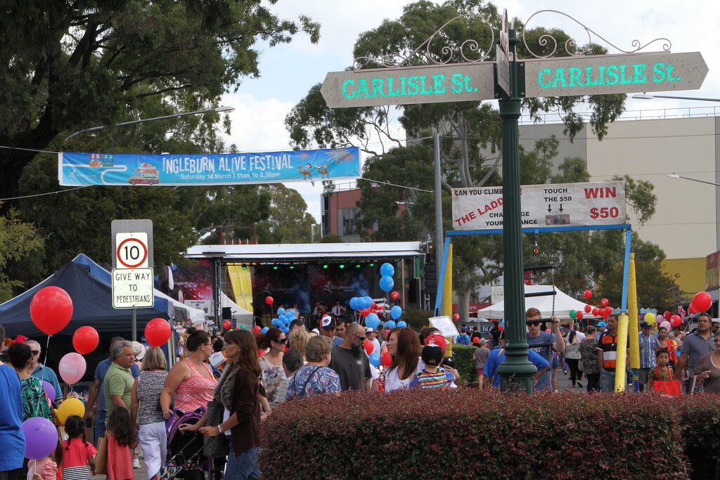 Crowds, balloons and a stage at the Ingleburn Alive festival, beneath the Carlisle Street sign