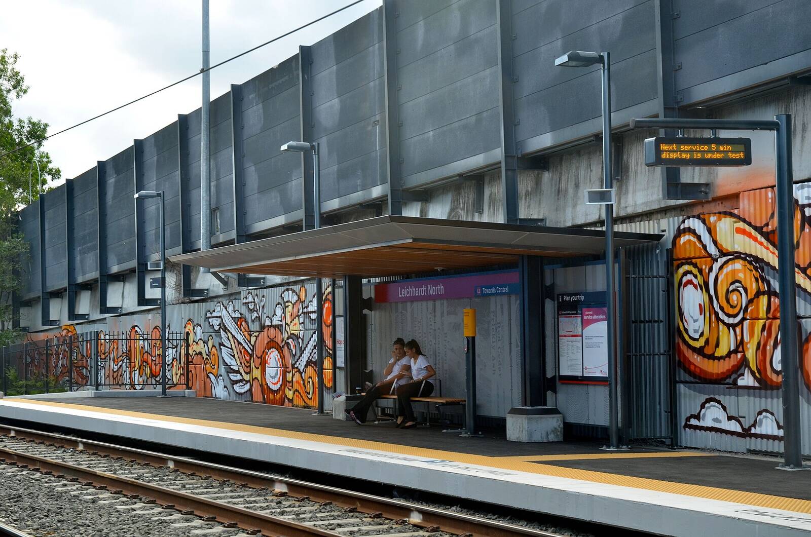 Leichhardt North light rail stop with its platform shelter and colourful murals on the wall behind