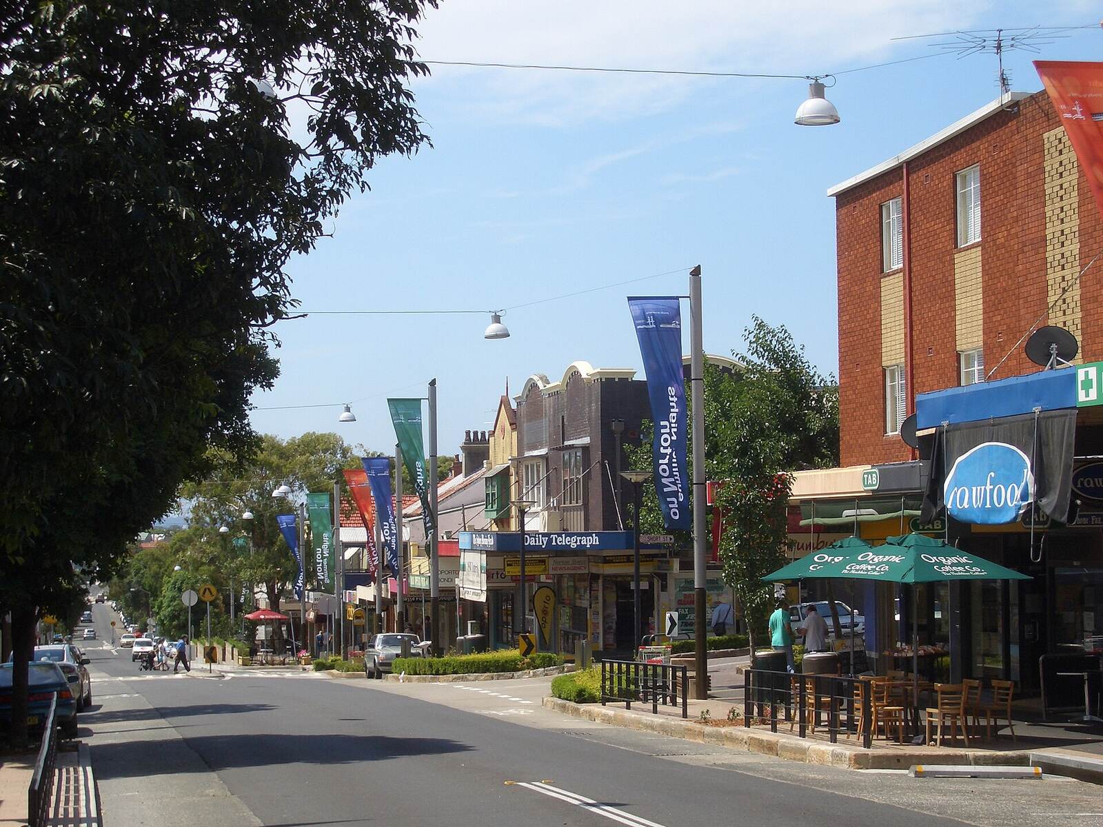 Norton Street in Leichhardt with street banners, shopfronts and outdoor cafe tables under green umbrellas