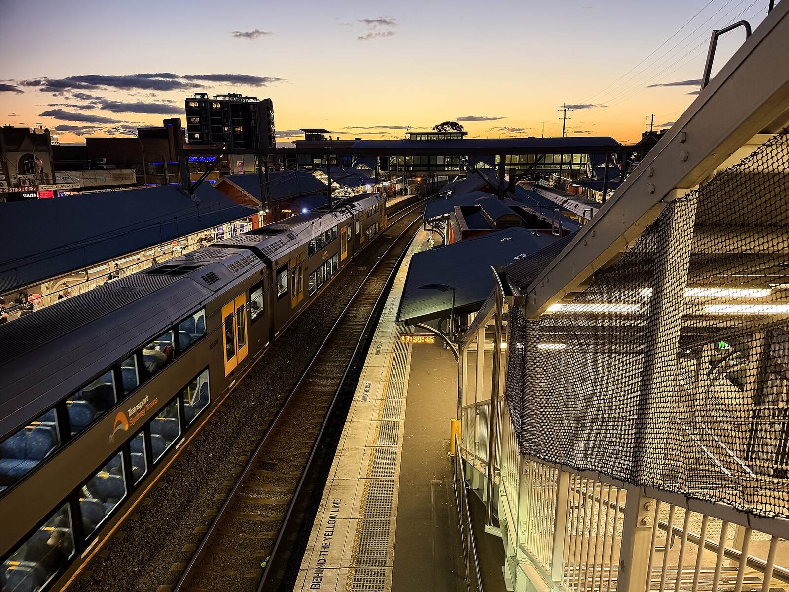 Lidcombe station platforms and a waiting double-decker train at sunset, seen from the footbridge