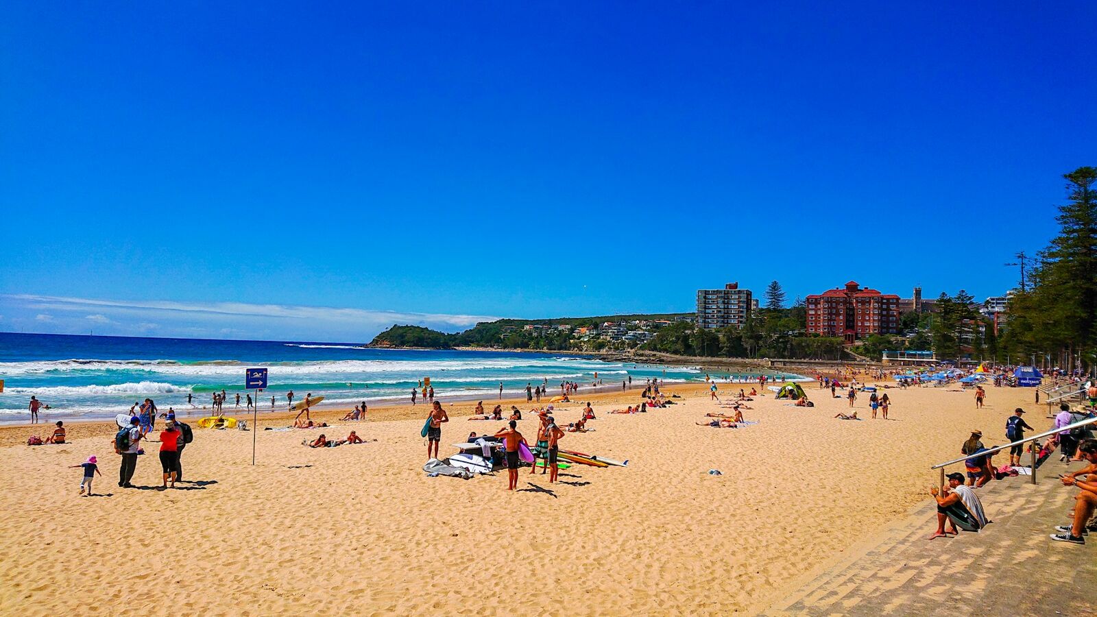 Swimmers and sunbathers on Manly Beach with apartments and headland behind