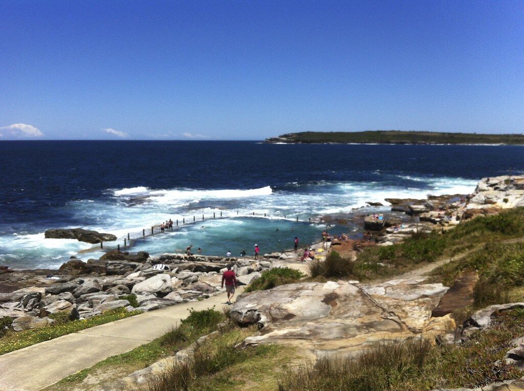 Swimmers at Mahon Pool, the ocean rock pool below the cliffs at north Maroubra, with a headland across the water