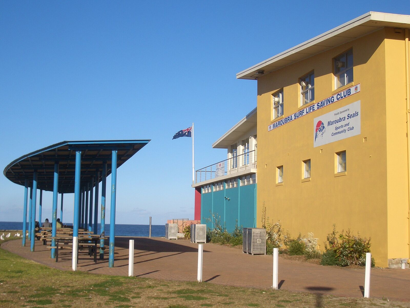Yellow Maroubra Surf Life Saving Club building and blue picnic shelter beside the beach