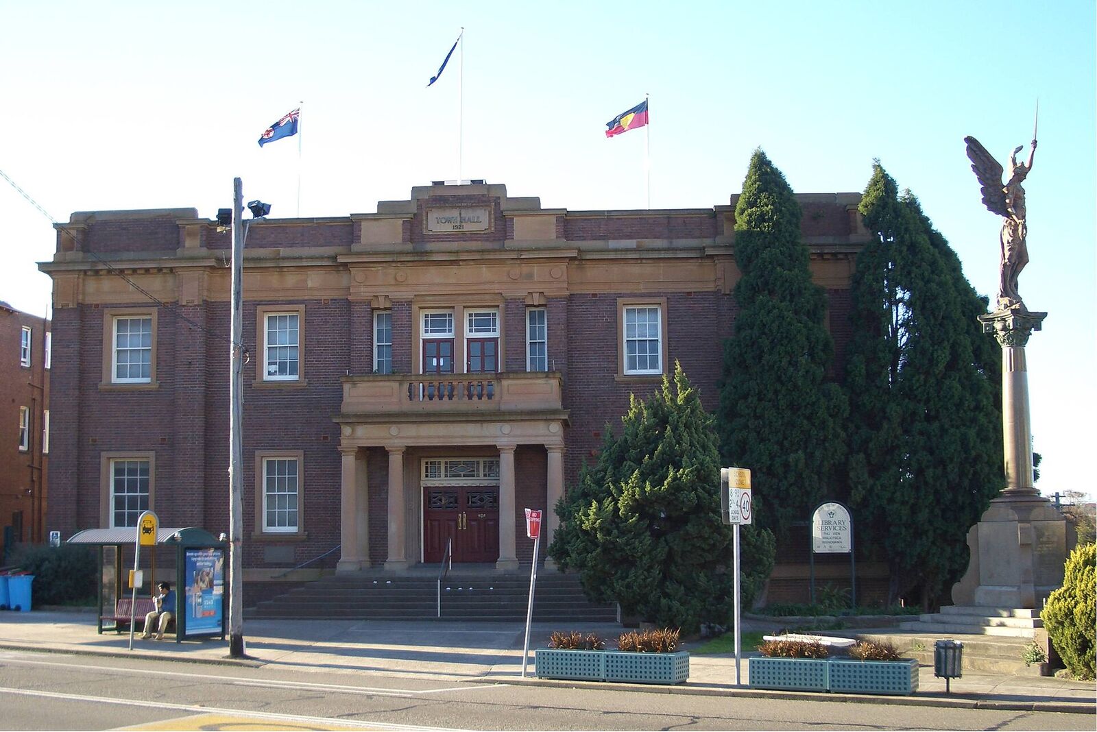 Marrickville Town Hall, a red brick building with flags, beside the Winged Victory war memorial statue