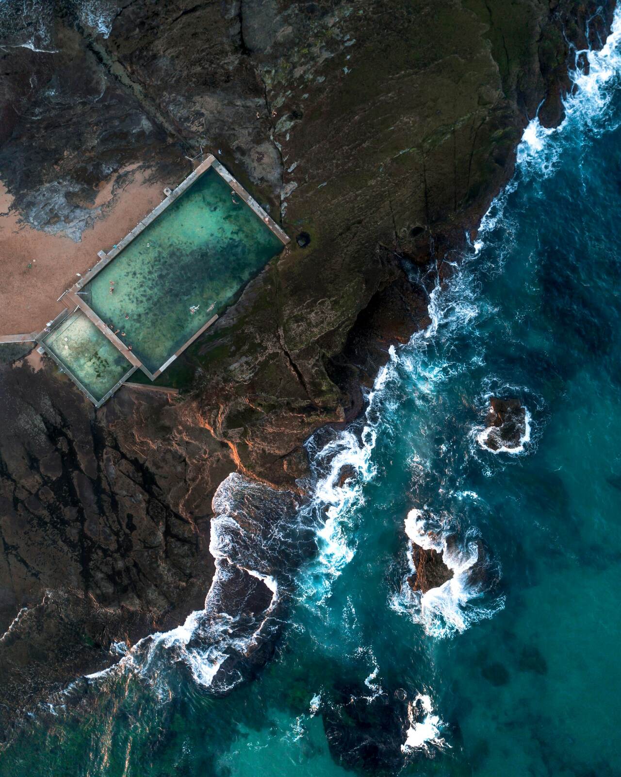 Aerial view of the Mona Vale rock pools on the rock shelf at the northern end of Mona Vale Beach, with surf around them