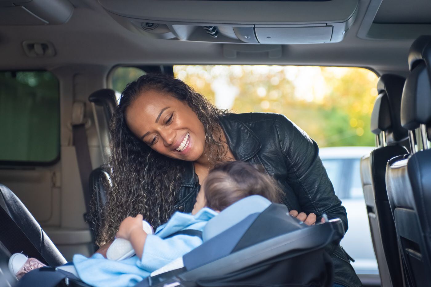 Smiling mother leaning into the back of a car to check on her baby in a car seat