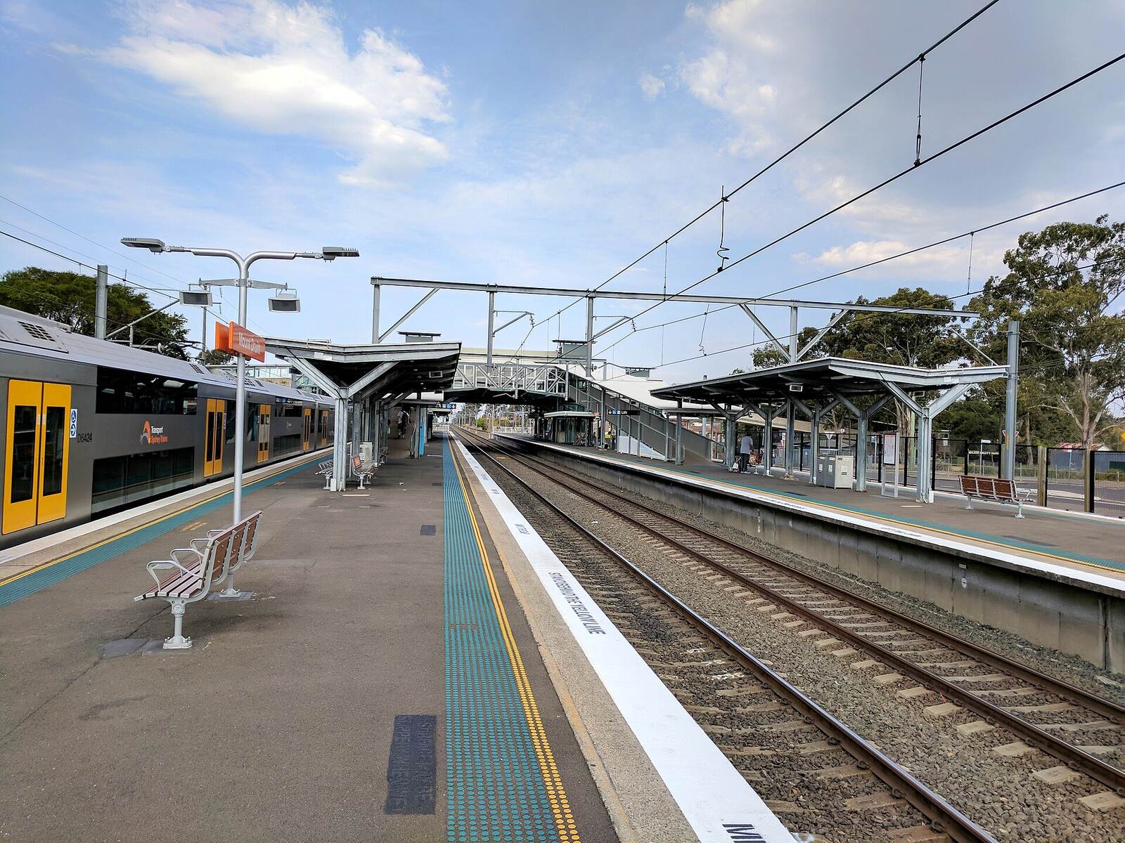 Mount Druitt station platforms under blue sky, with a Sydney Trains carriage at the platform and the footbridge ahead