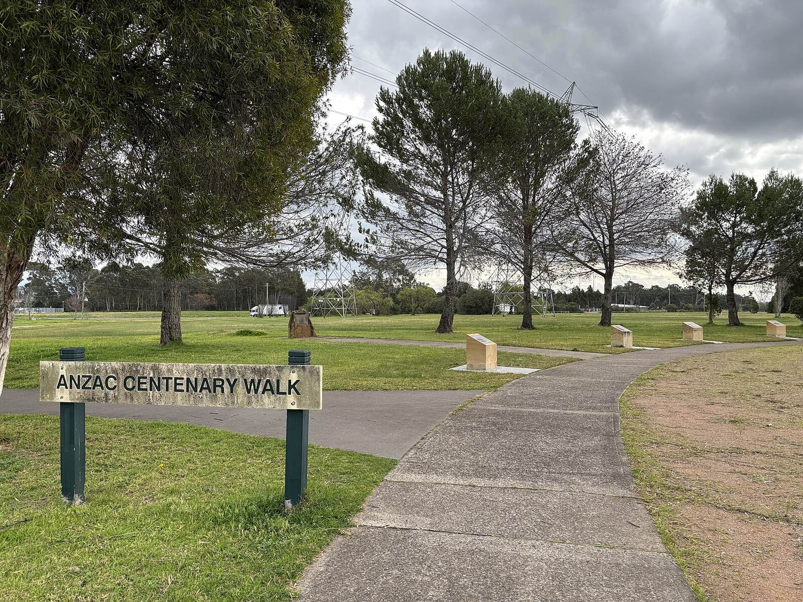 Anzac Centenary Walk sign and path through lawn and pine trees at the Mount Druitt Waterholes Remembrance Garden