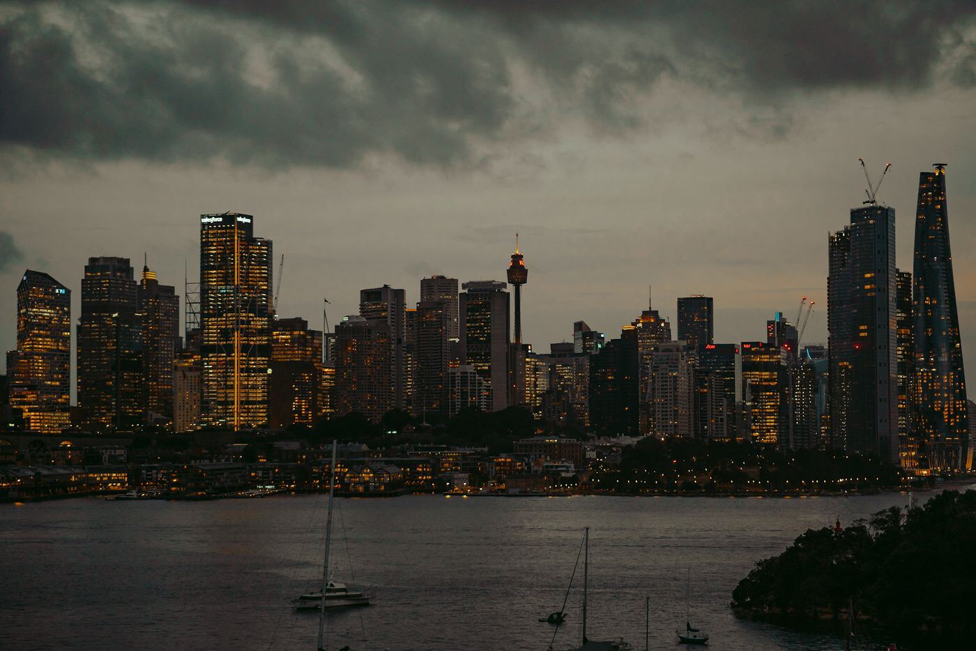 City skyline lit up at dusk across the harbour under heavy cloud