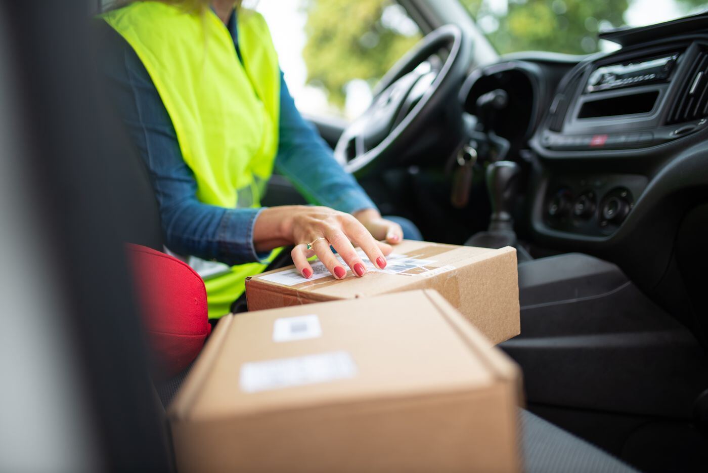 Driver in a high-visibility vest placing parcels on the passenger seat of a vehicle