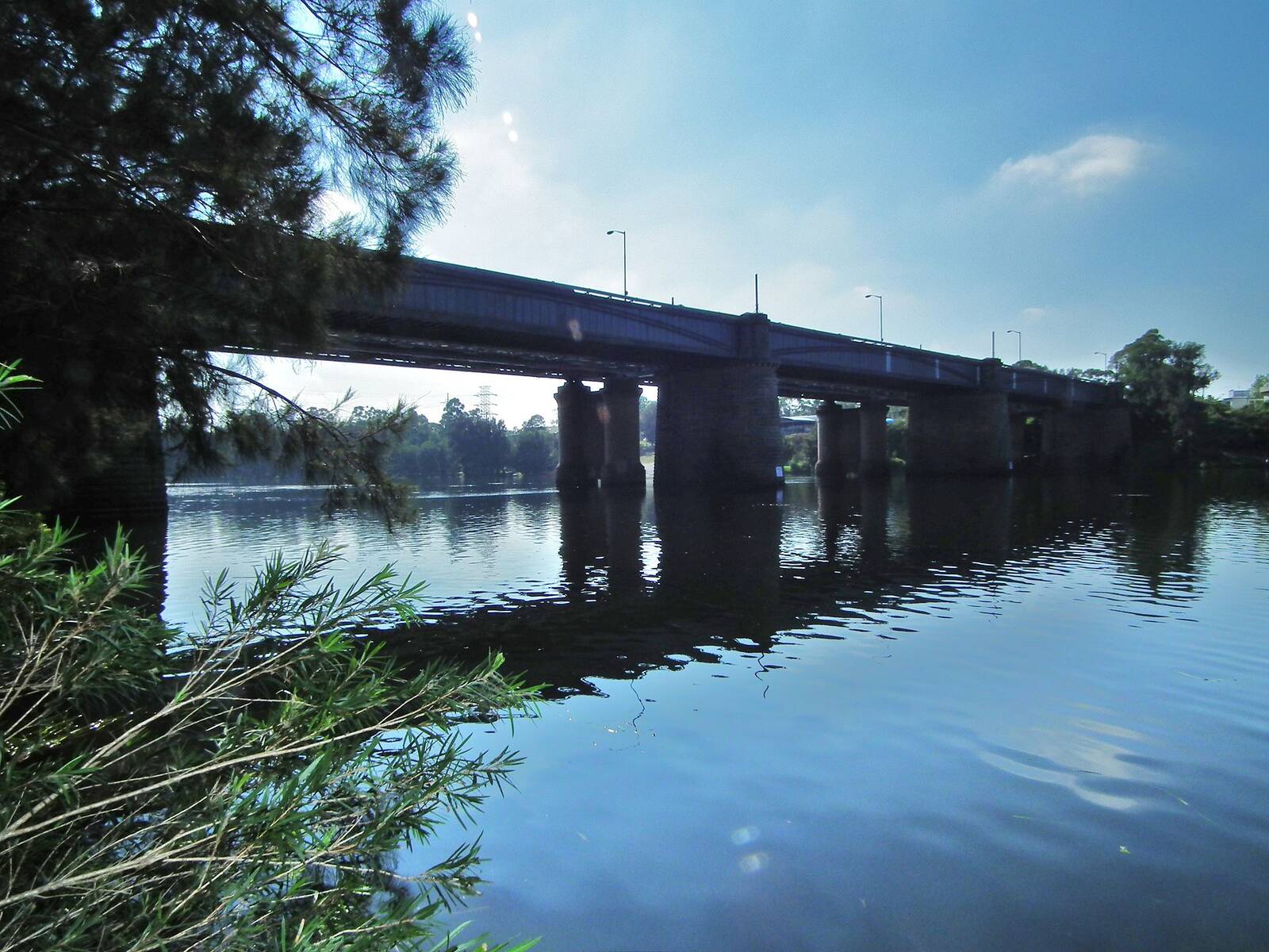 Sandstone piers of the Victoria Bridge crossing the calm Nepean River at Penrith, framed by casuarina branches