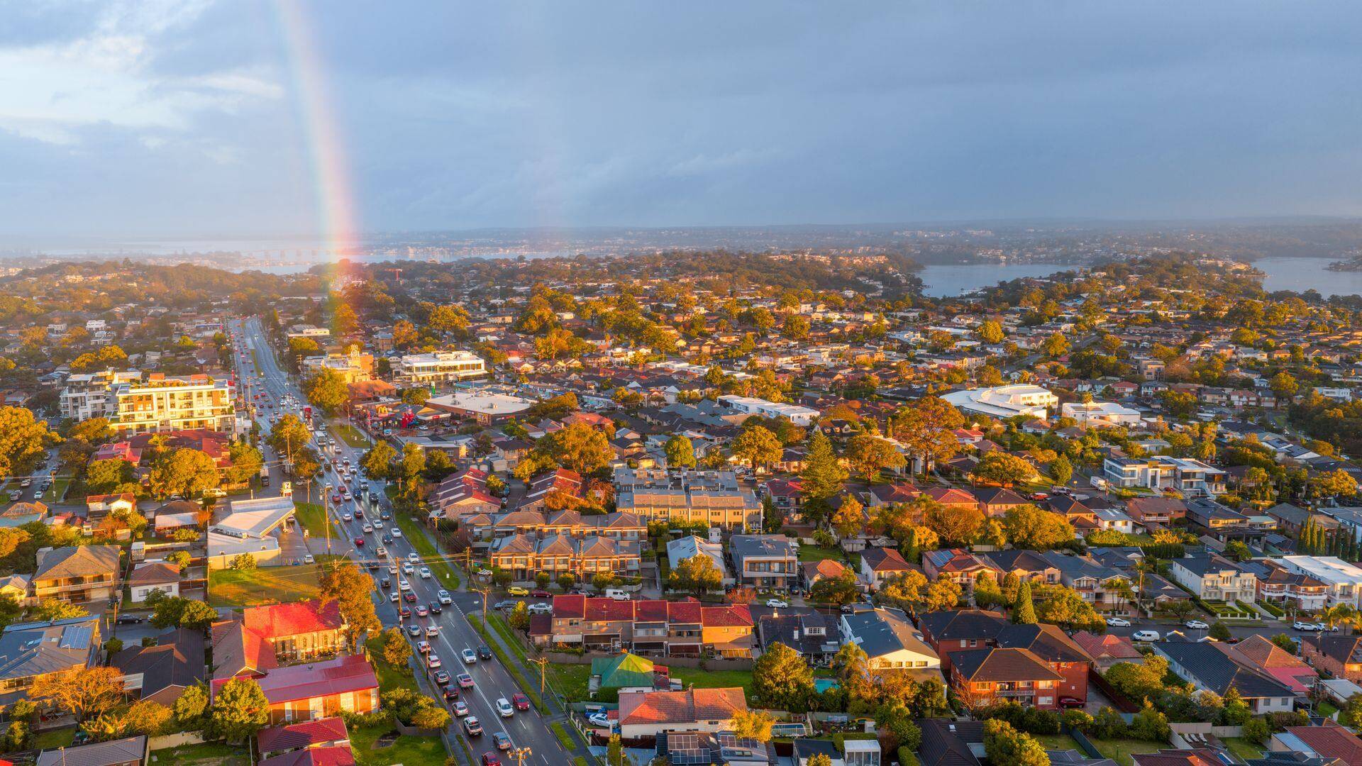 Rainbow over suburban Sydney rooftops and a busy main road at sunset