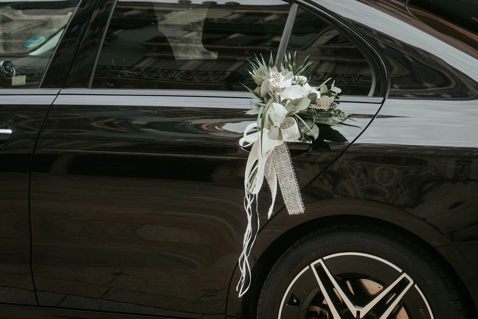 White flowers and ribbon tied to the rear door of a black sedan for a wedding