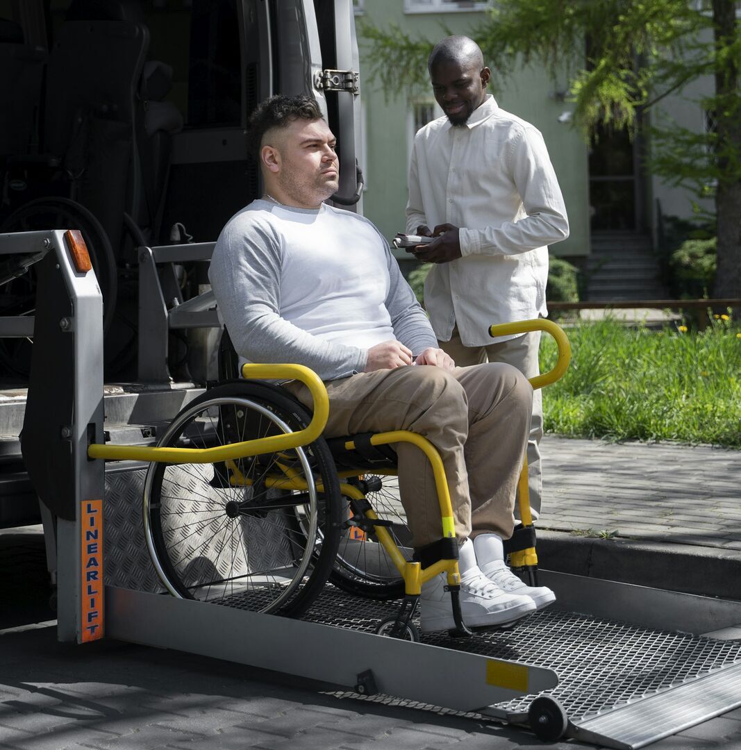 Man in a wheelchair on the lowered platform lift of a van while a helper stands beside him