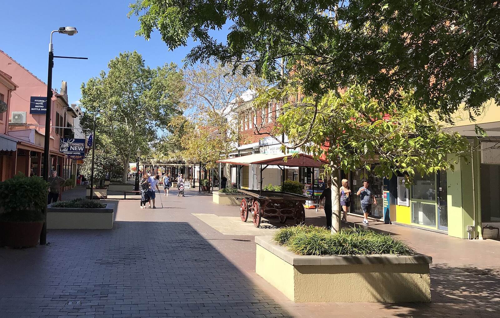 Paved pedestrian mall on George Street, Windsor, with shade trees, planters and an old timber cart
