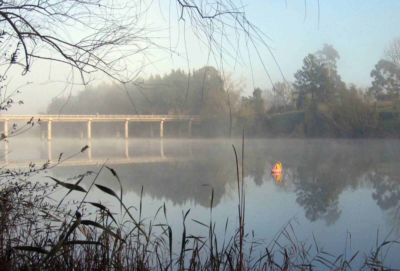 Morning mist over a still stretch of the Hawkesbury River at Windsor, with the old low-level bridge in the distance